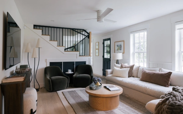 Living room arrangement with curved sofa, round wood coffee table, green accent chairs, and staircase backdrop